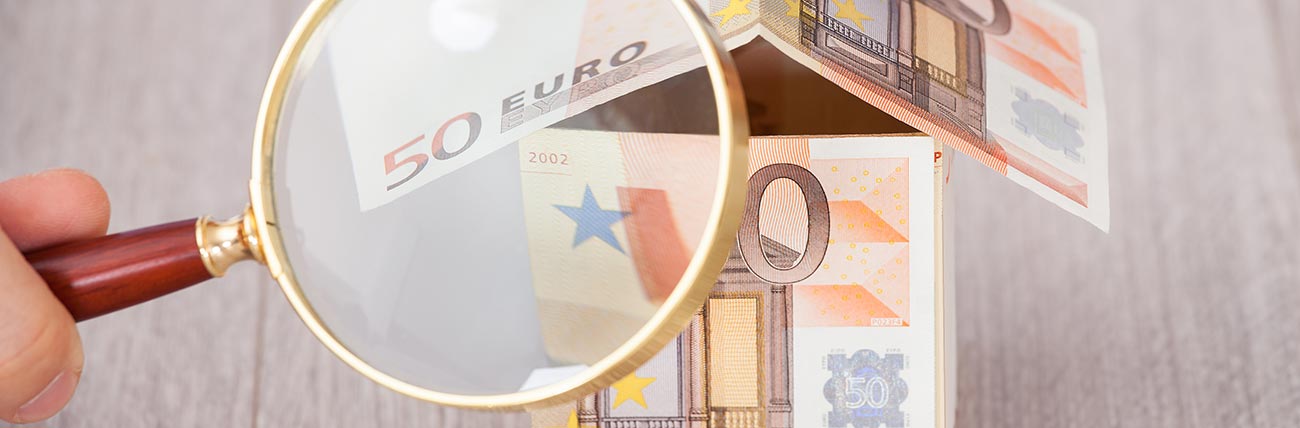 Lente d'ingrandimento sopra a due banconote da 50 euro sistemate a forma di casa